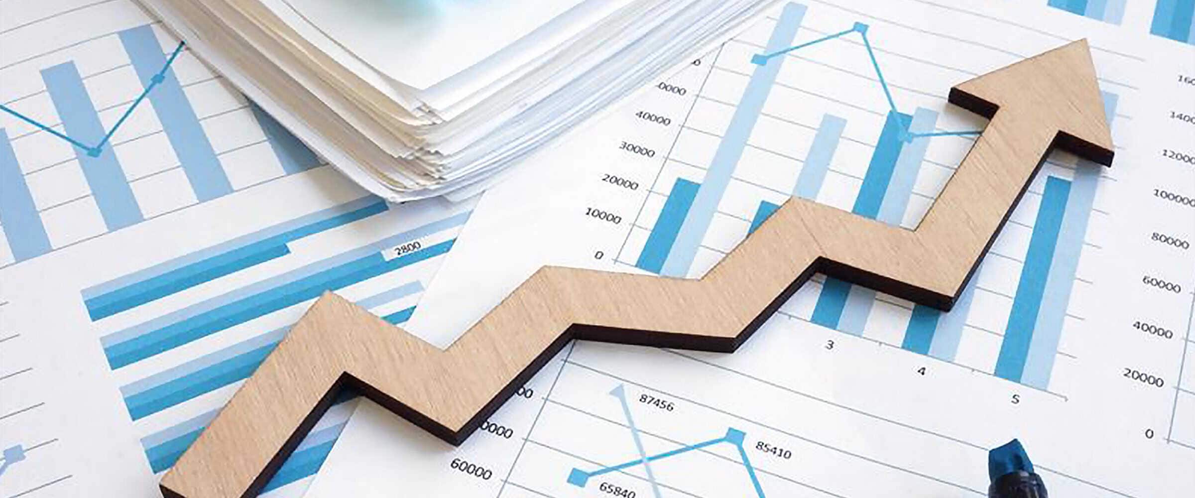 Several sheets of paper with graphs and charts on them with a large growth arrow icon on top of them.